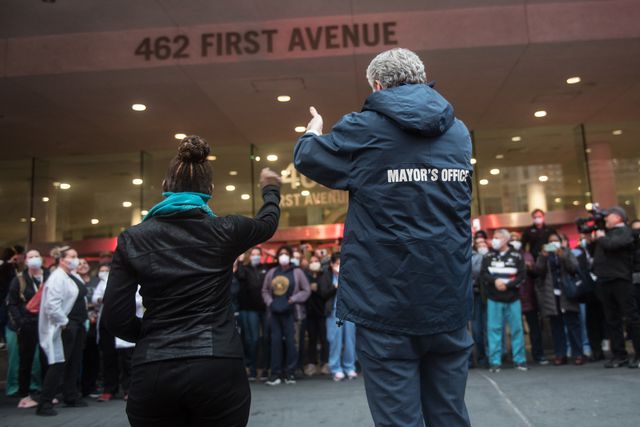A photographer showing the backs of Mayor Bill de Blasio and First Lady Chirlane McCray as they clap for hospital workers at Bellevue Hosiptal